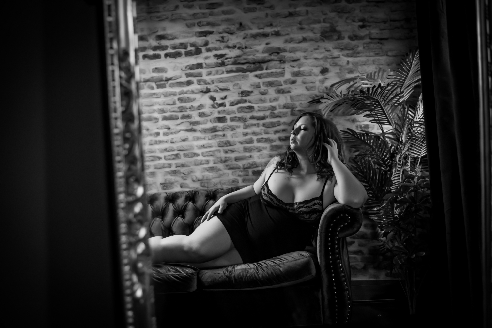 A woman in black lingerie poses on a couch in the rochester new york boudoir studio.