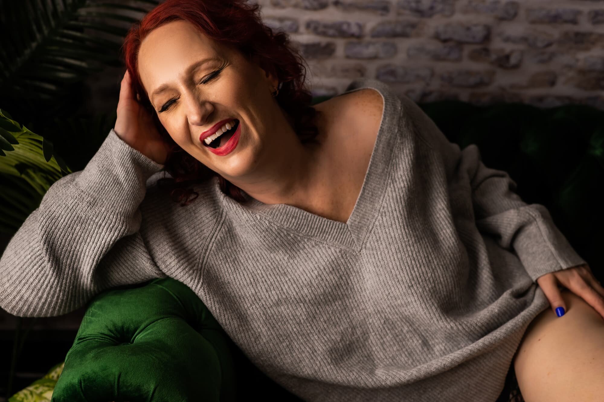 A woman laughing in a sweater at a boudoir studio in rochester new york.