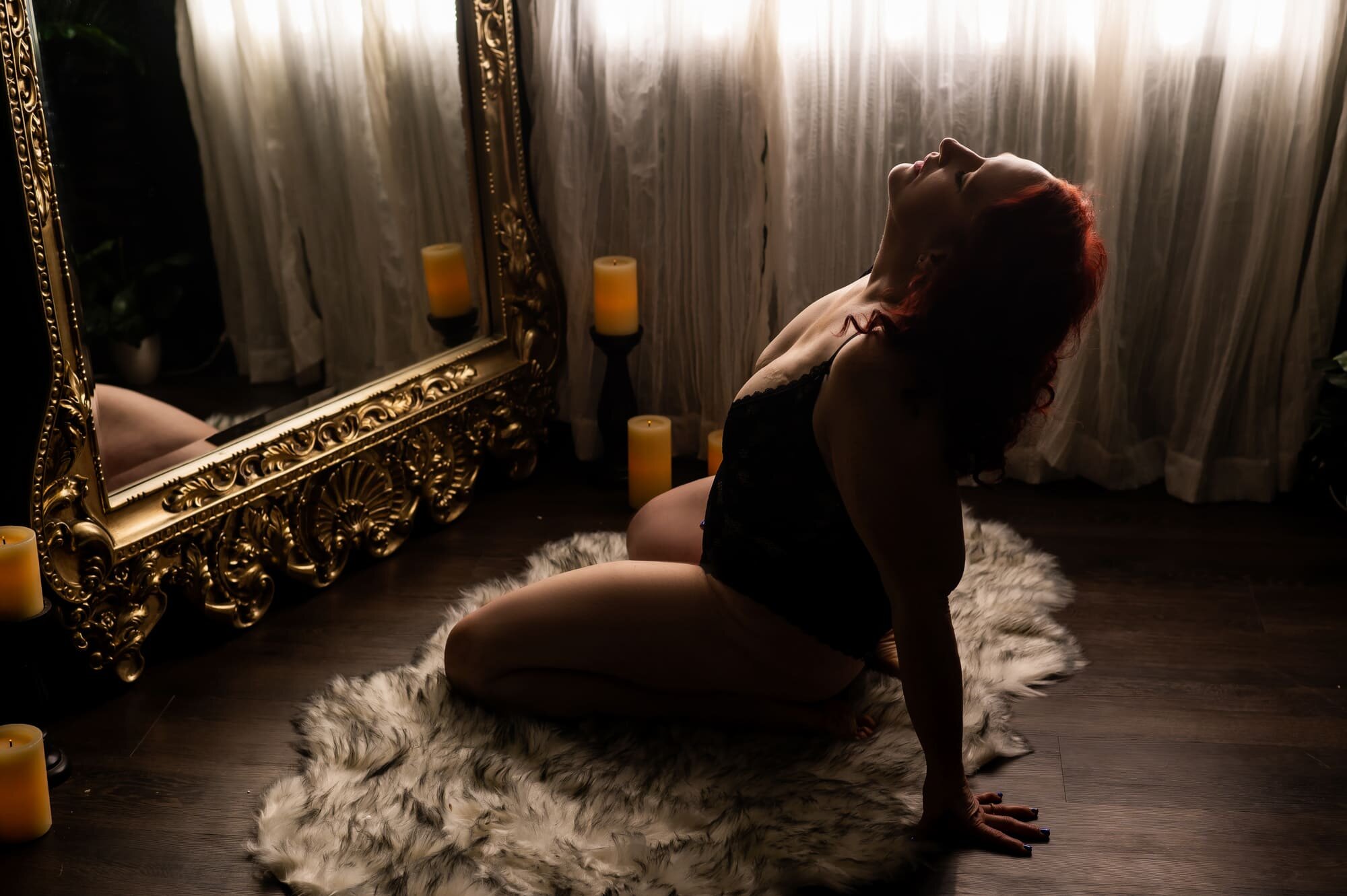 A woman in black lingerie poses in front of a mirror at a boudoir studio in rochester new york.